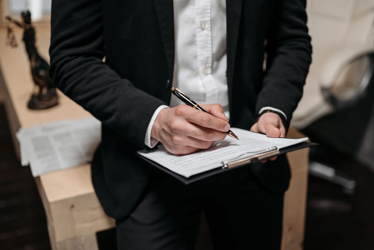 A lawyer in a dark suit signing a document on a clipboard