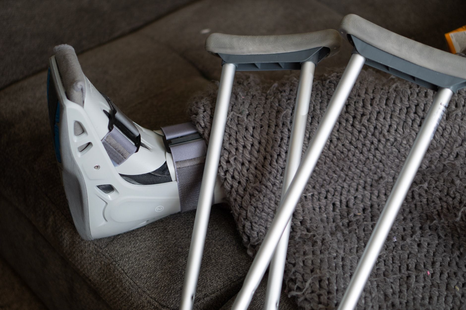 An orthopedic walking boot and crutches resting on a couch during recovery
